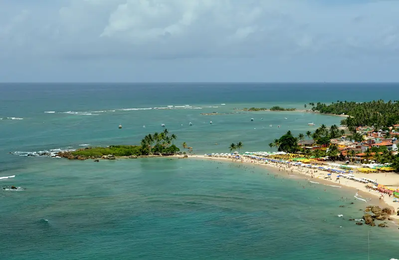 Vista do alto da Segunda Praia de Morro de São Paulo, com guarda-sóis na areia, a Ilha da Saudade coberta de coqueiros e o mar verde
