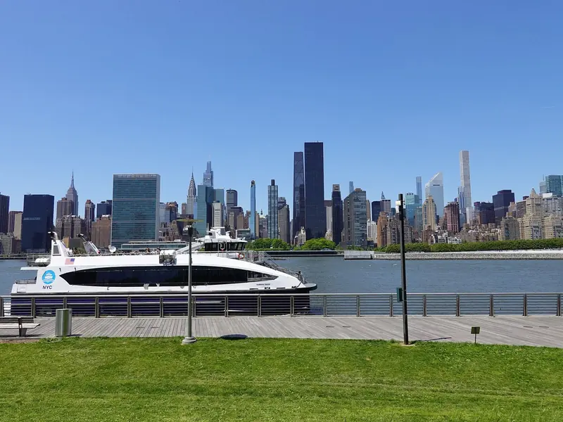 Barco do NYC Ferry passando diante do Gantry Plaza State Park, com o horizonte de Midtown do outro lado do East River