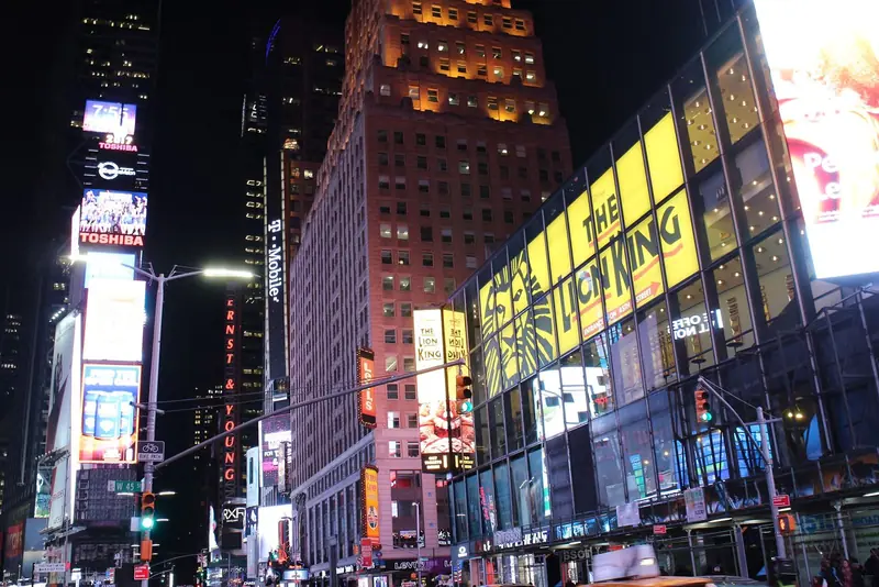 Fachadas iluminadas de Times Square à noite, com letreiros de teatro e telões nos prédios
