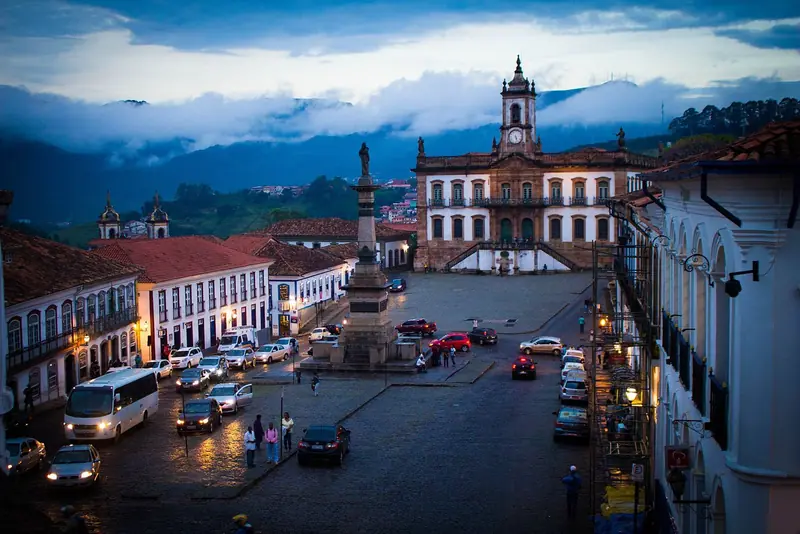 Praça Tiradentes ao entardecer, com o monumento a Tiradentes, o Museu da Inconfidência e as serras cobertas de nuvens ao fundo