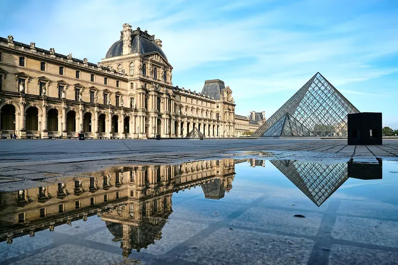 Ala Denon do Louvre e a pirâmide de vidro refletidas numa poça no pátio, de manhã cedo