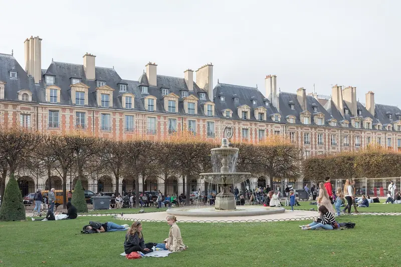 Place des Vosges com prédios de tijolo e telhados de ardósia, chafariz no centro e gente sentada na grama