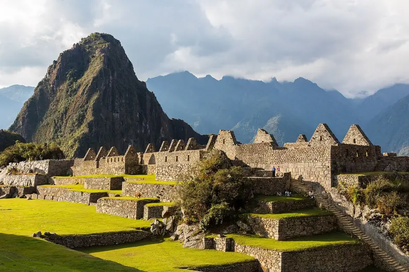 Casas de pedra de Machu Picchu com empenas triangulares, terraços gramados e o pico de Huayna Picchu ao fundo