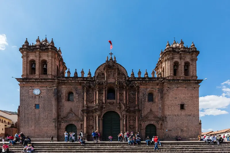 Fachada de pedra da Catedral de Cusco, com duas torres sineiras e escadaria cheia de gente na Plaza de Armas