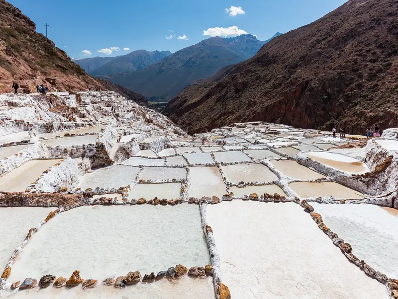 Tanques de sal brancos e retangulares das Salineras de Maras, separados por bordas de pedra, descendo pelas encostas de um cânion seco