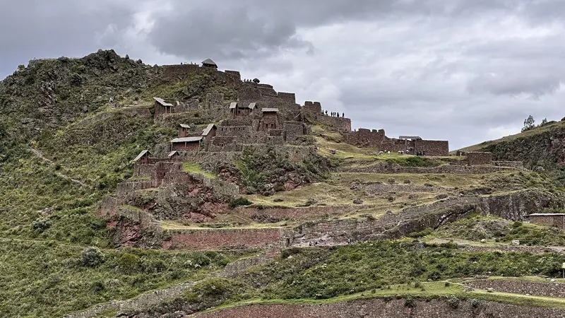 Ruínas incas de Pisac no alto de uma crista verde, com muros de pedra, casas restauradas com telhados novos e terraços descendo pela encosta