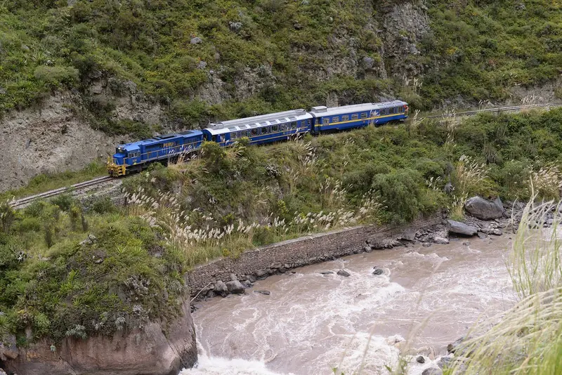 Trem azul da PeruRail passando numa encosta de mata sobre as corredeiras do Rio Urubamba