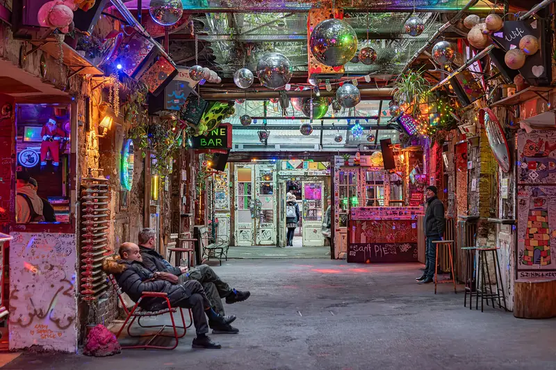 Corredor interno do Szimpla Kert com globos espelhados no teto, luzes coloridas, paredes grafitadas e cadeiras de ferro