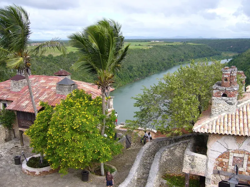 Casas de pedra com telhado de barro e árvore de flores amarelas no alto de um morro, com o rio Chavón correndo entre a mata ao fundo
