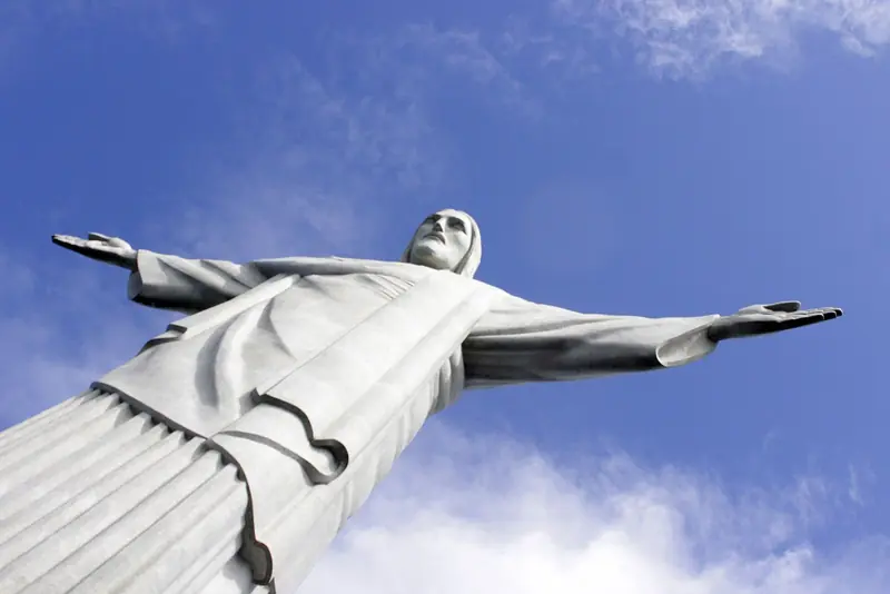 Estátua do Cristo Redentor de braços abertos vista de baixo, contra o céu azul