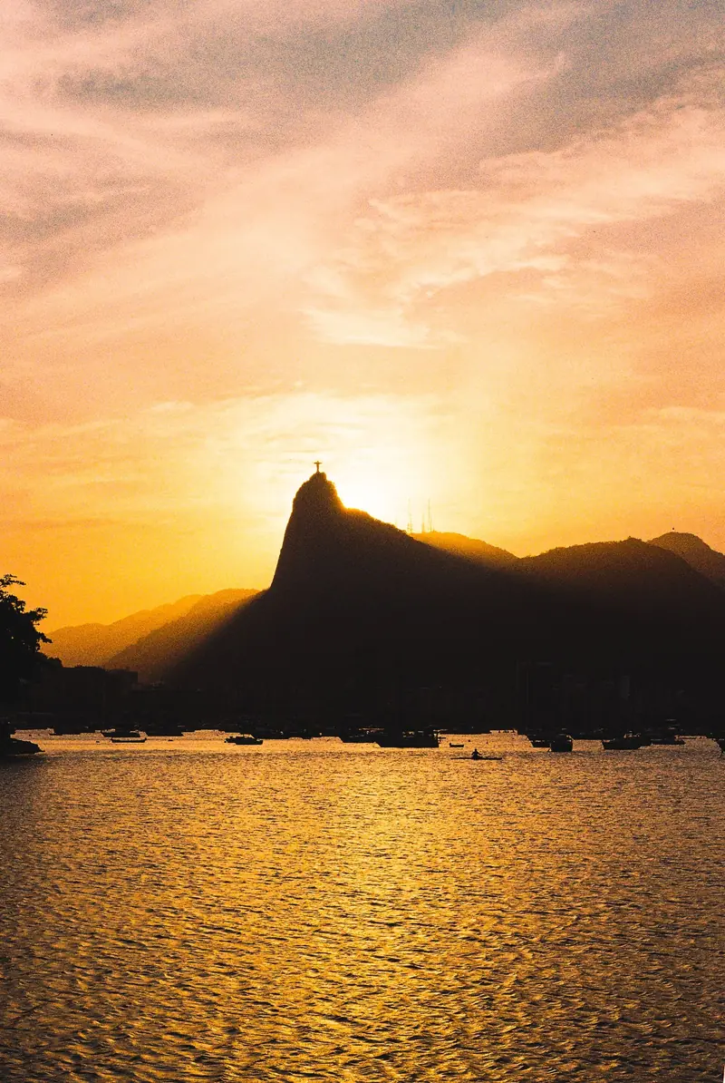 Silhueta do Corcovado com o Cristo ao pôr do sol, vista da Urca sobre a água