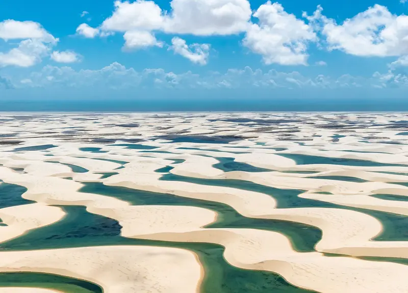 Vista aérea de dunas brancas com lagoas verdes e azuis entre elas, no Parque Nacional dos Lençóis Maranhenses