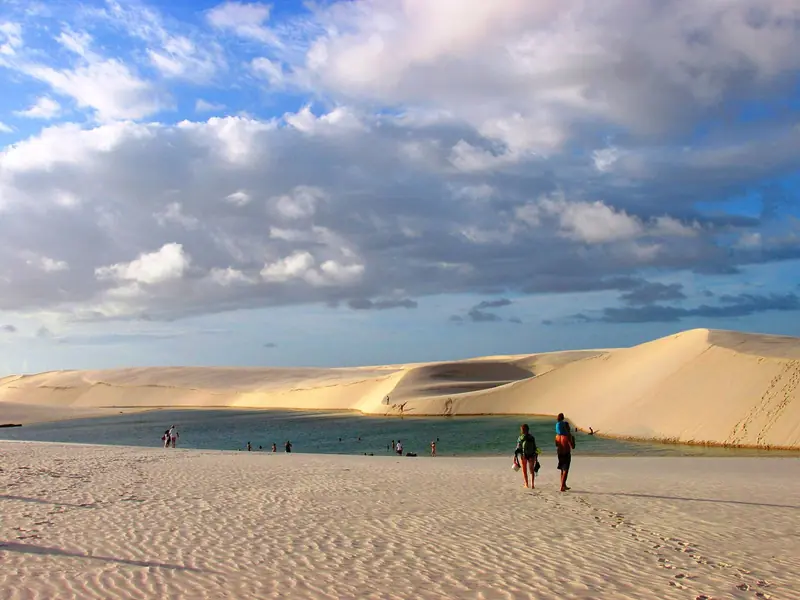 Lagoa entre dunas altas, com algumas pessoas caminhando pela areia, perto de Barreirinhas