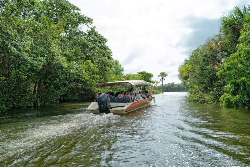 Lancha com turistas subindo um trecho estreito do Rio Preguiças, com mata dos dois lados