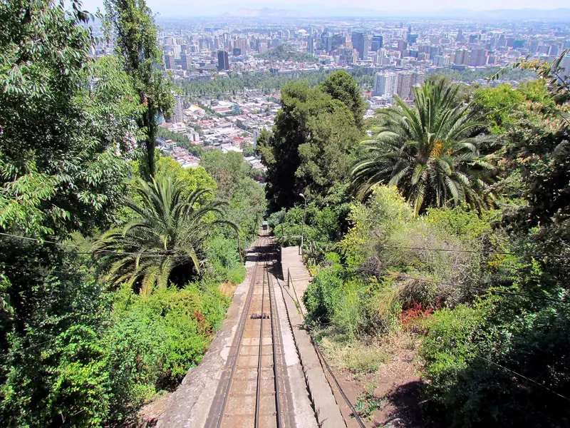 Trilho do funicular descendo o Cerro San Cristóbal entre palmeiras, com a cidade de Santiago ao fundo