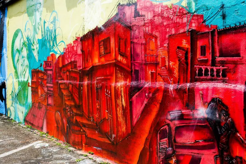 Muro do Beco do Batman pintado com casarios vermelhos, ao lado do calçamento do beco