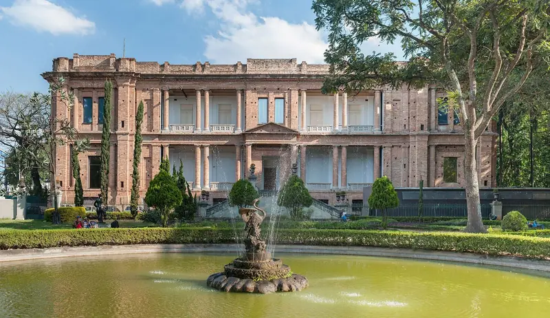 Fachada de tijolos da Pinacoteca vista do jardim, com chafariz em primeiro plano