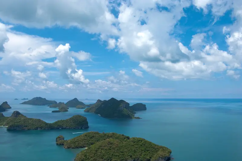 Ilhas de calcário cobertas de mata espalhadas num mar azul, vistas do alto, sob nuvens brancas
