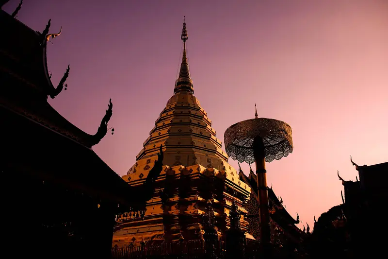 Silhueta dos telhados do Wat Phra That Doi Suthep e o chedi dourado contra o céu rosado do entardecer