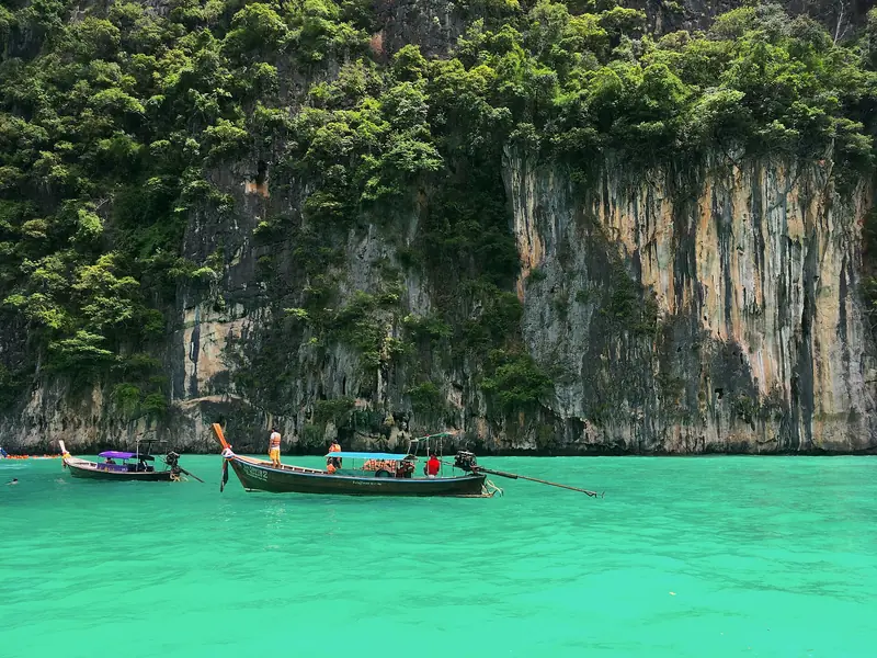 Barco de cauda longa na água verde-esmeralda da lagoa de Pileh, sob um paredão de calcário coberto de mata