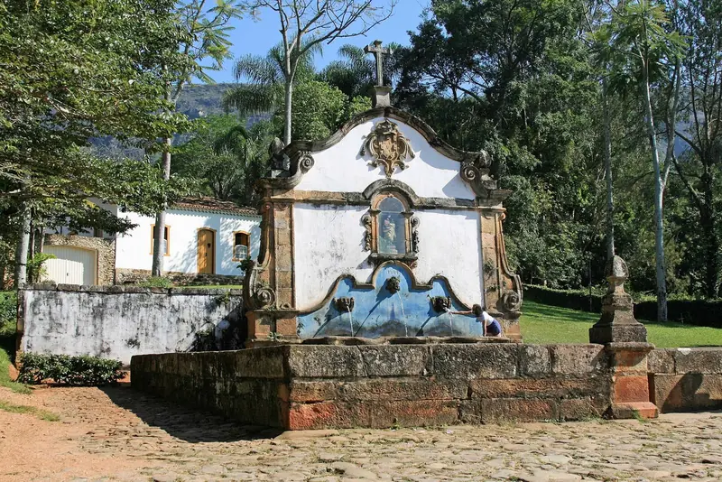 Chafariz de São José, com frontão branco e painel azul, cercado de árvores