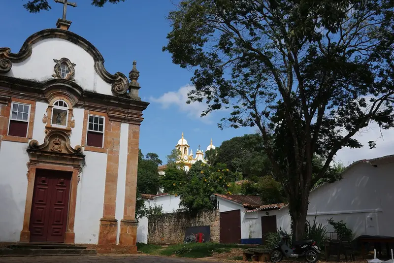 Igreja do Rosário dos Pretos, de fachada branca e pedra, com as torres da Matriz ao fundo