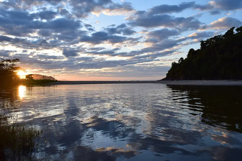 Rio Itamambuca ao amanhecer, com o céu refletido na água e a mata do costão à direita